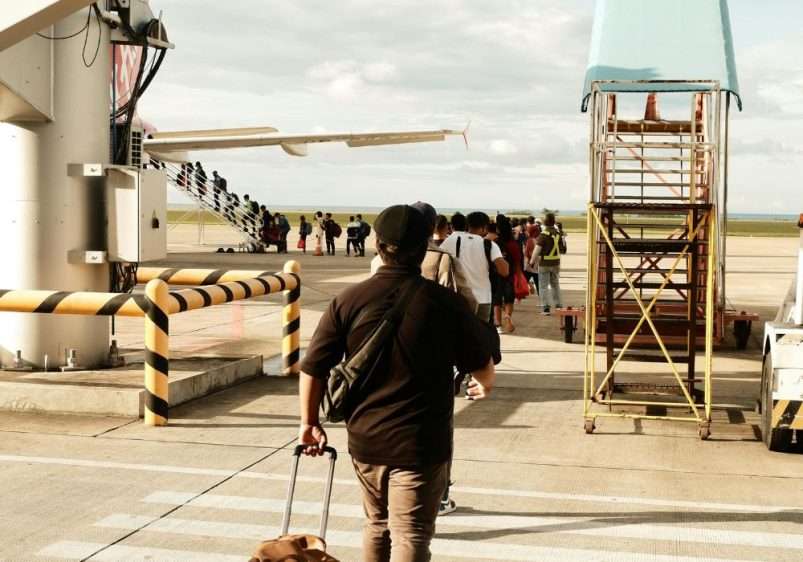 Travellers boarding plane via outdoor stairway at airport.